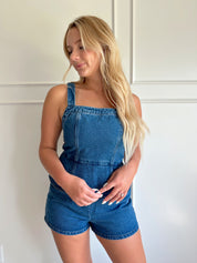Dark wash denim peplum romper with self tie back closure.