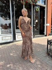 Woman wearing leopard maxi dress with v-neckline and adjustable straps.