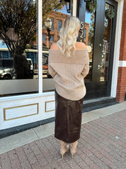 Woman wearing oversized, off the shoulder, tan sweater with brown leather skirt. 