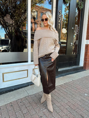 Woman wearing oversized, off the shoulder, tan sweater with brown leather skirt. 