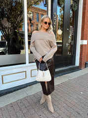 Woman wearing oversized, off the shoulder, tan sweater with brown leather skirt. 