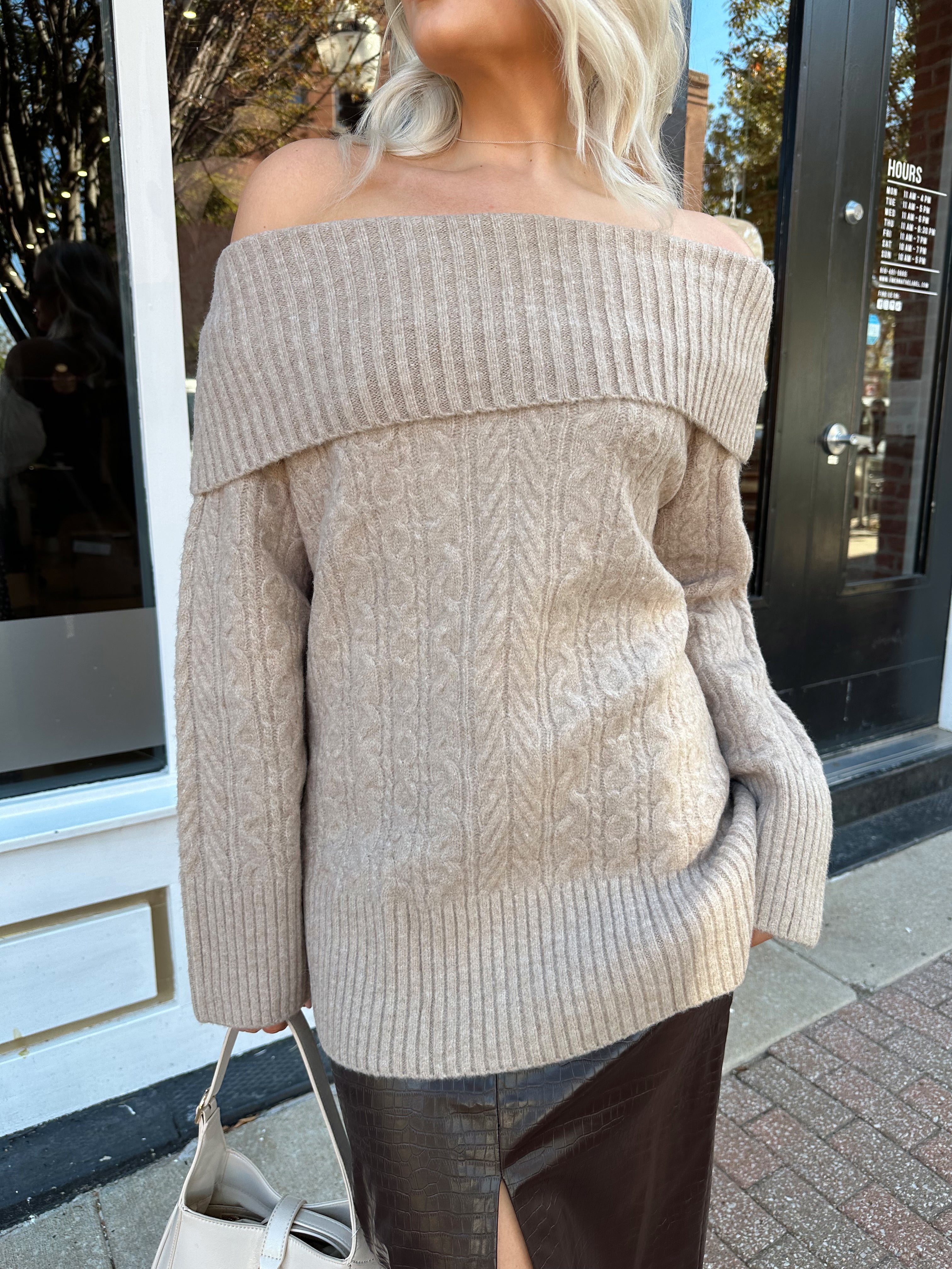 Woman wearing oversized, off the shoulder, tan sweater with brown leather skirt. 
