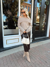 Woman wearing oversized, off the shoulder, tan sweater with brown leather skirt. 