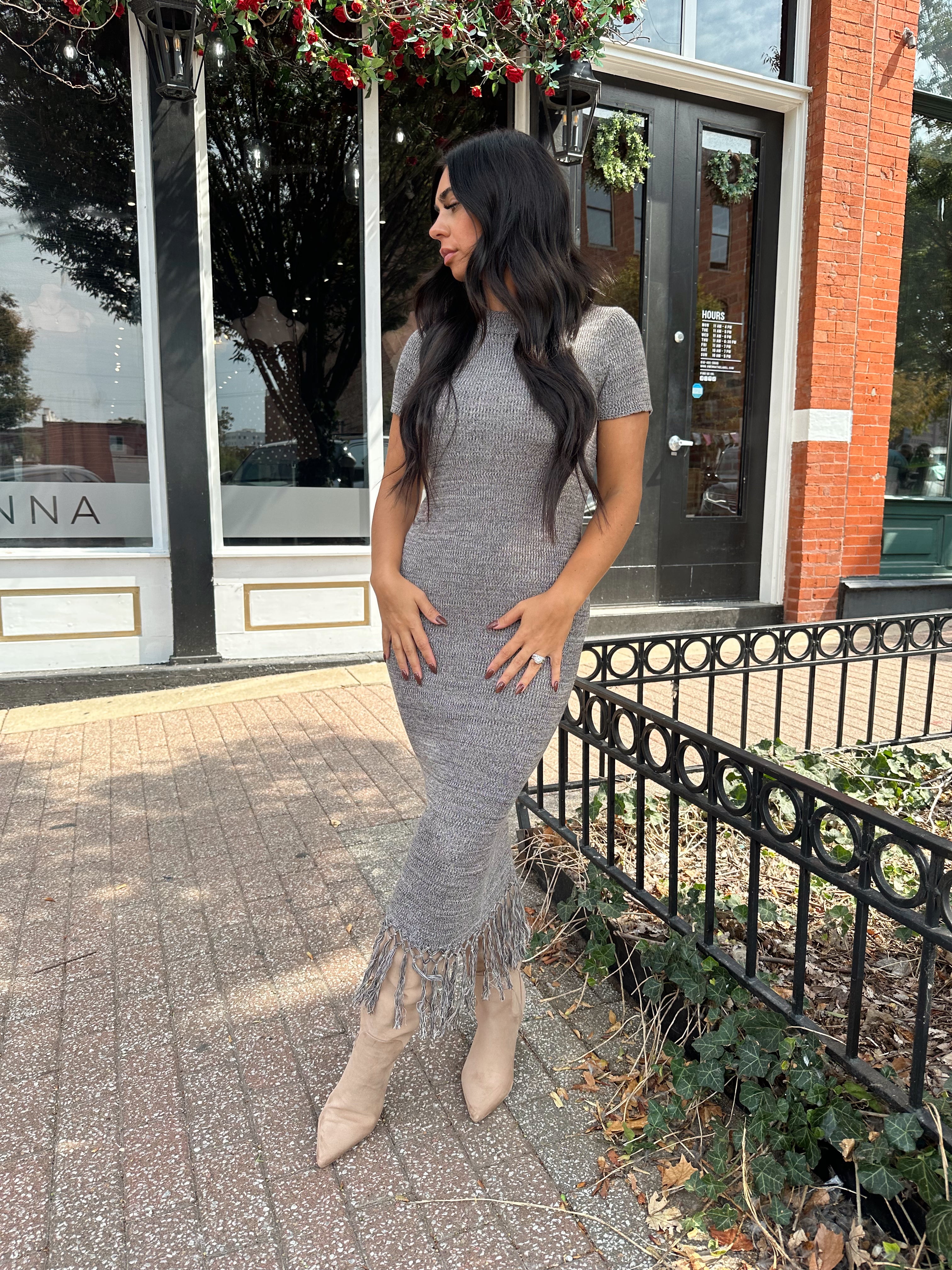 Woman wearing charcoal grey midi dress with fringe hem bottom and short sleeves.
