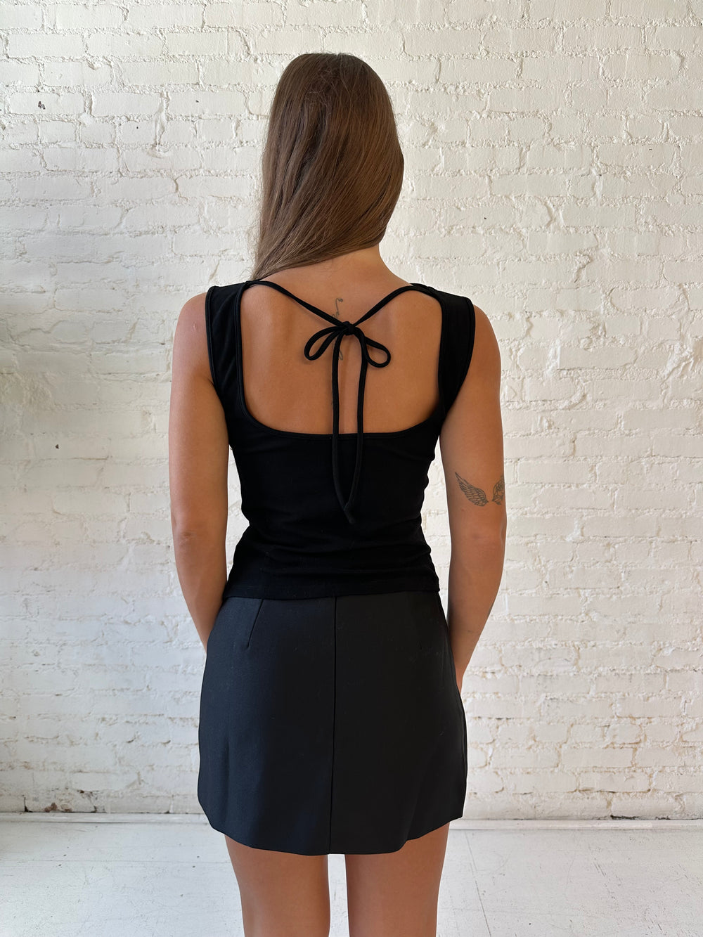 Woman wearing black knit high neck top with cowl neckline and open tie back. 