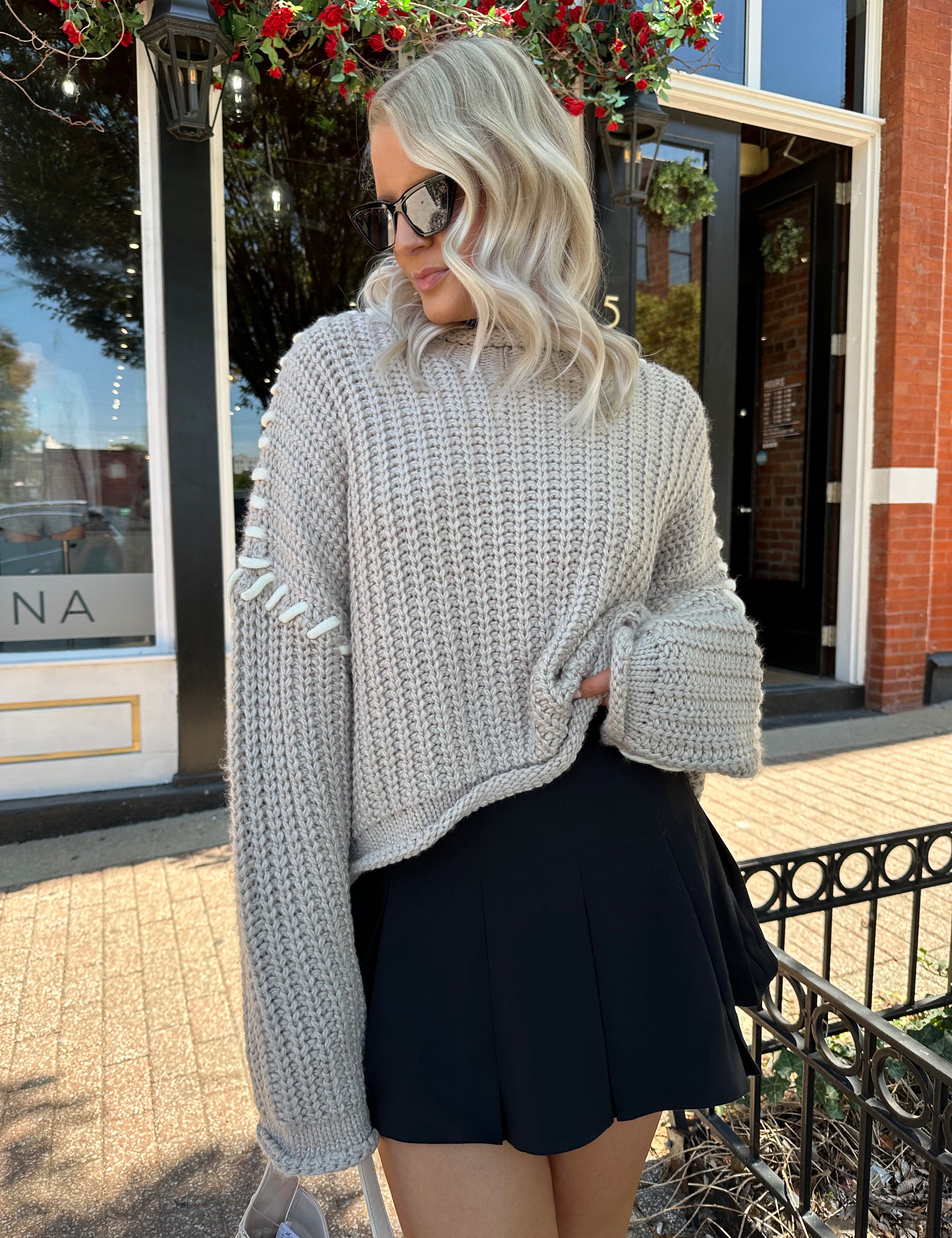 Woman wearing a grey knit oversized sweater with contrast lacing. 