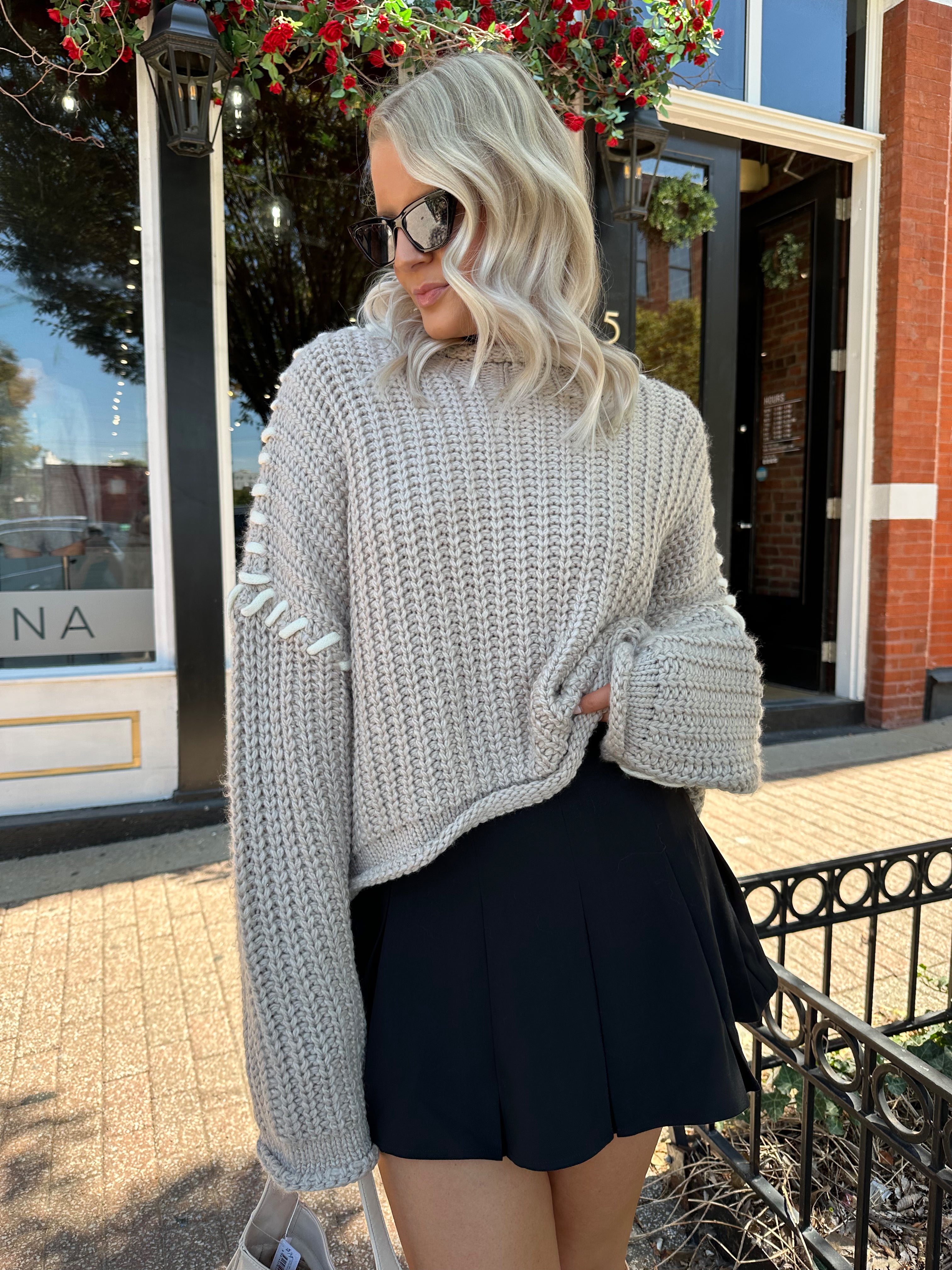 Woman wearing a grey knit oversized sweater with contrast lacing. 