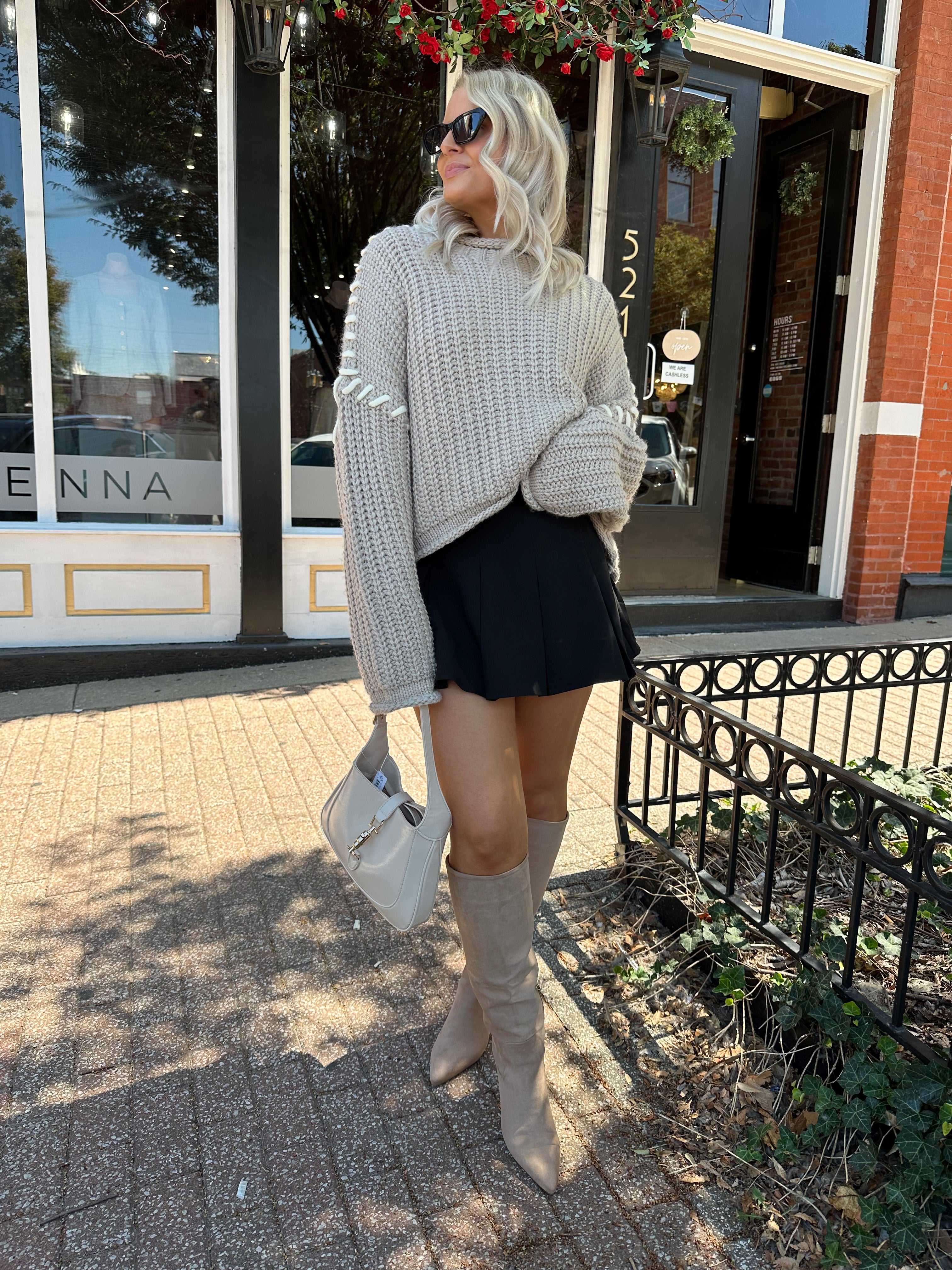 Woman wearing a grey knit oversized sweater with contrast lacing. 