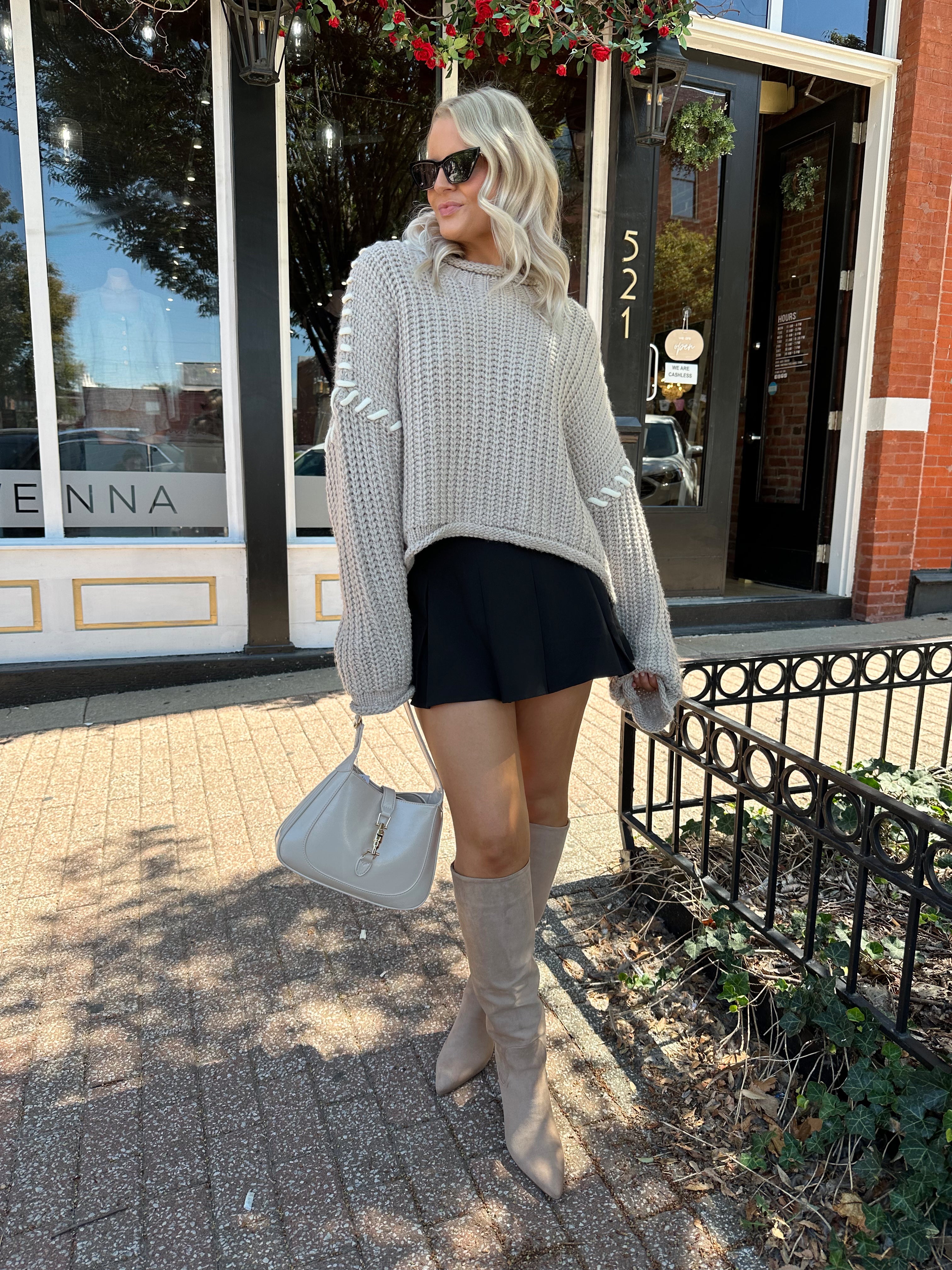 Woman wearing a grey knit oversized sweater with contrast lacing. 