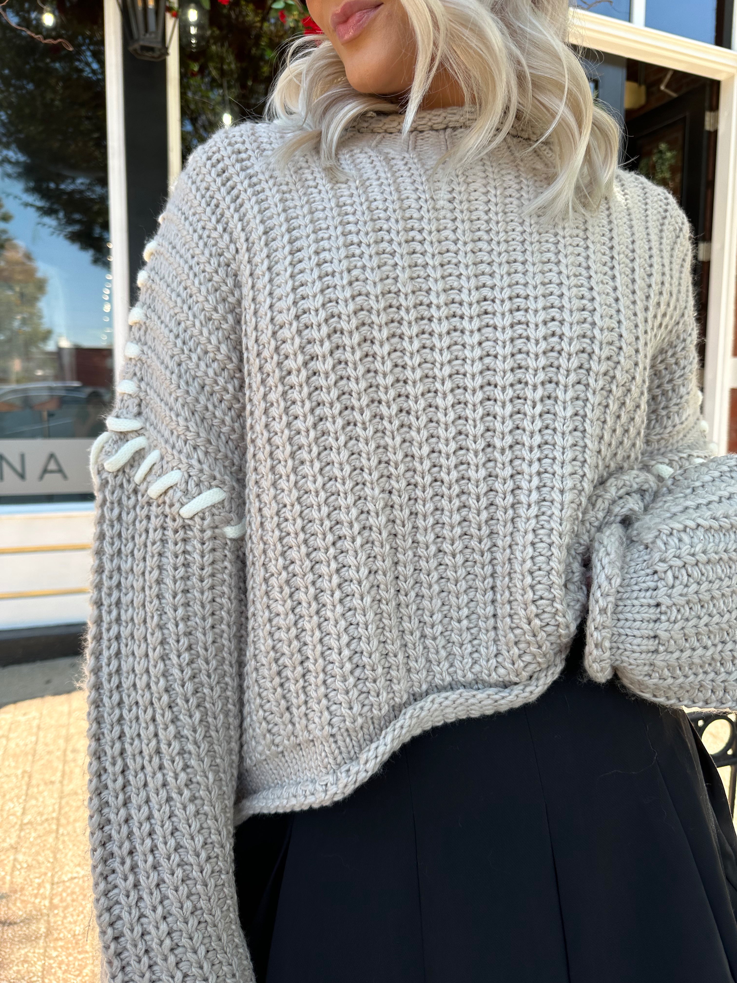 Woman wearing a grey knit oversized sweater with contrast lacing. 