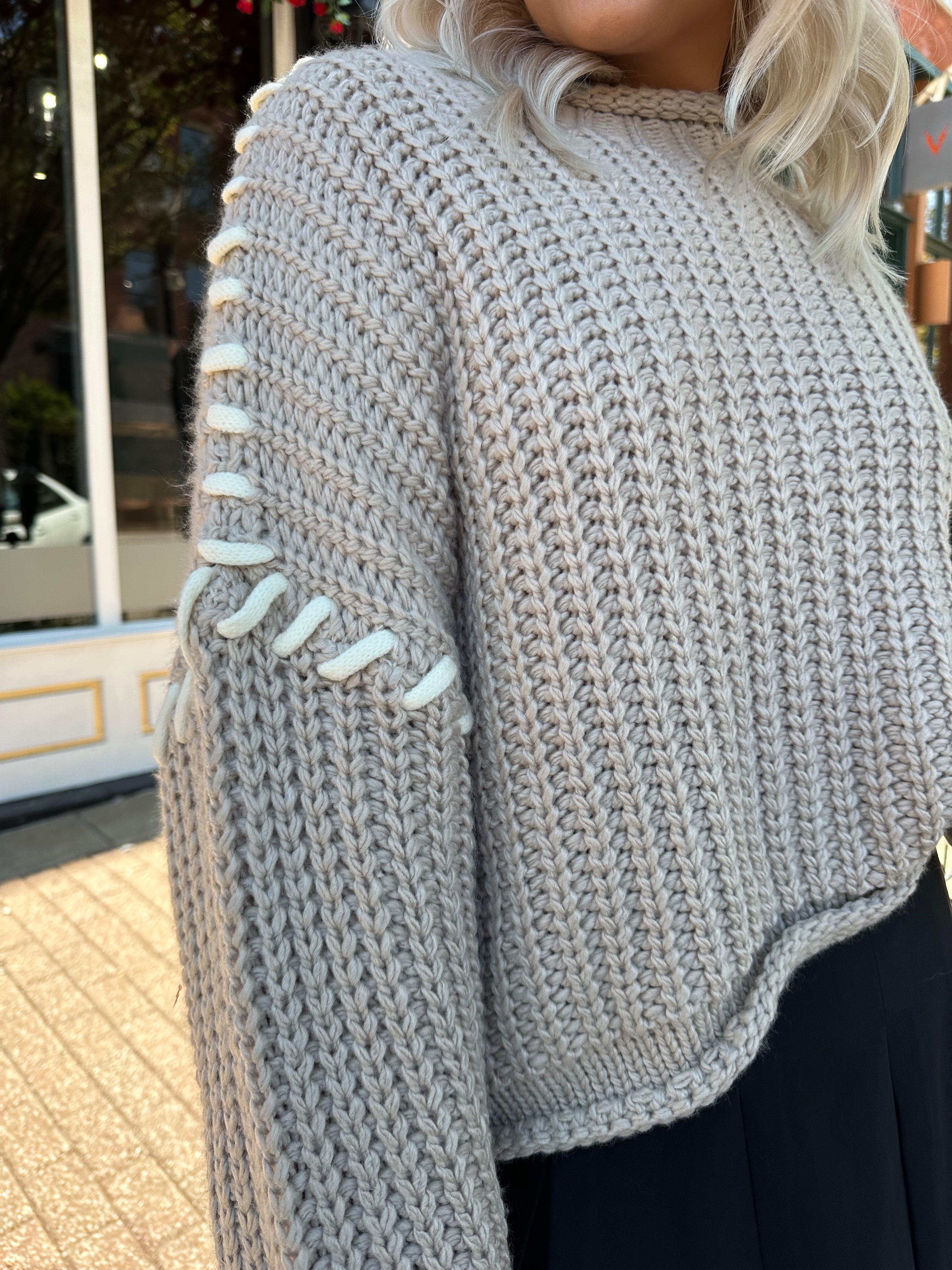 Woman wearing a grey knit oversized sweater with contrast lacing. 