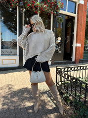 Woman wearing a grey knit oversized sweater with contrast lacing. 