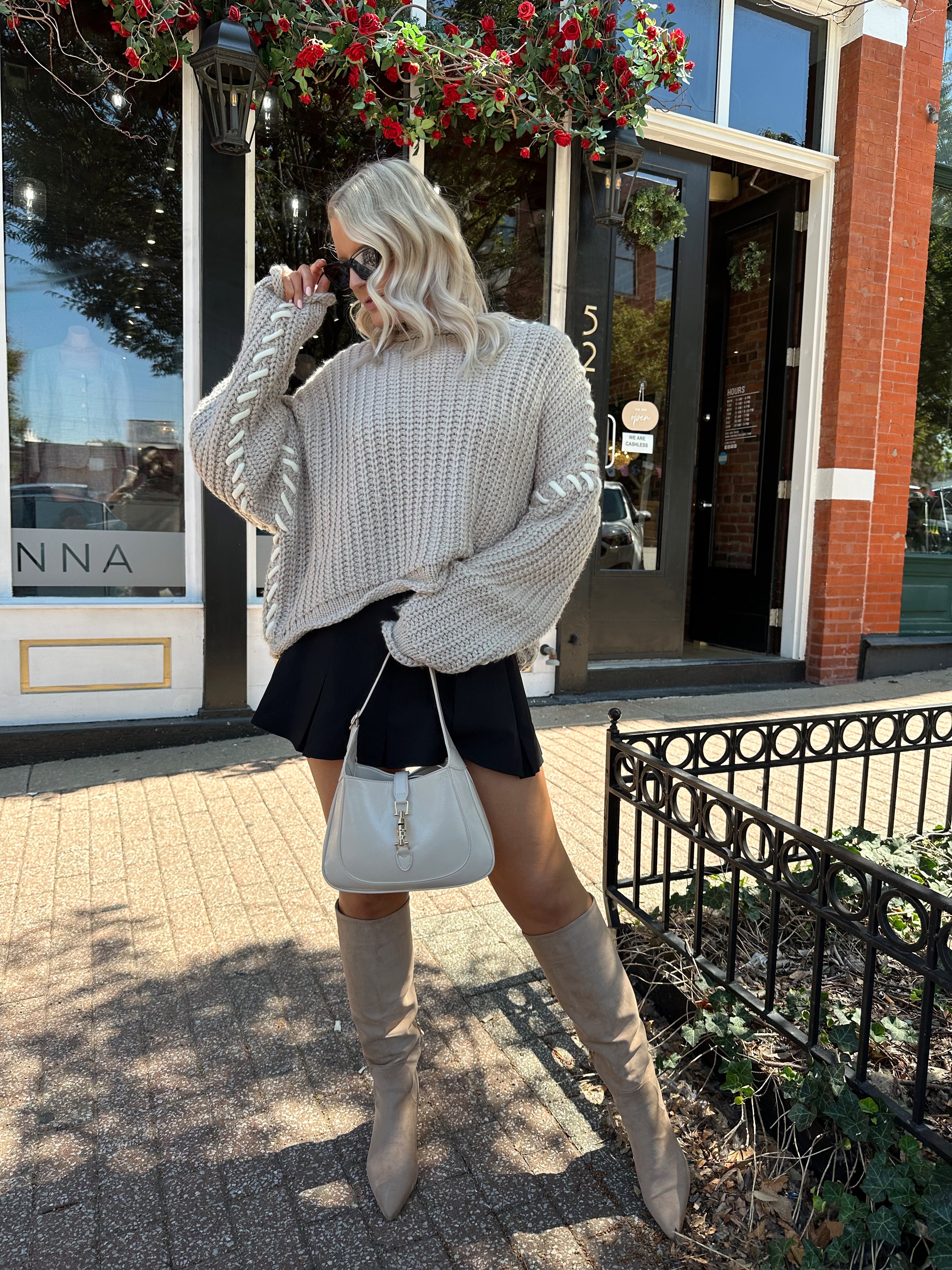 Woman wearing a grey knit oversized sweater with contrast lacing. 