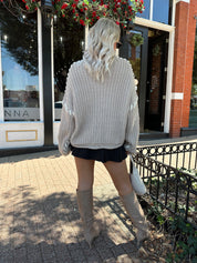 Woman wearing a grey knit oversized sweater with contrast lacing. 