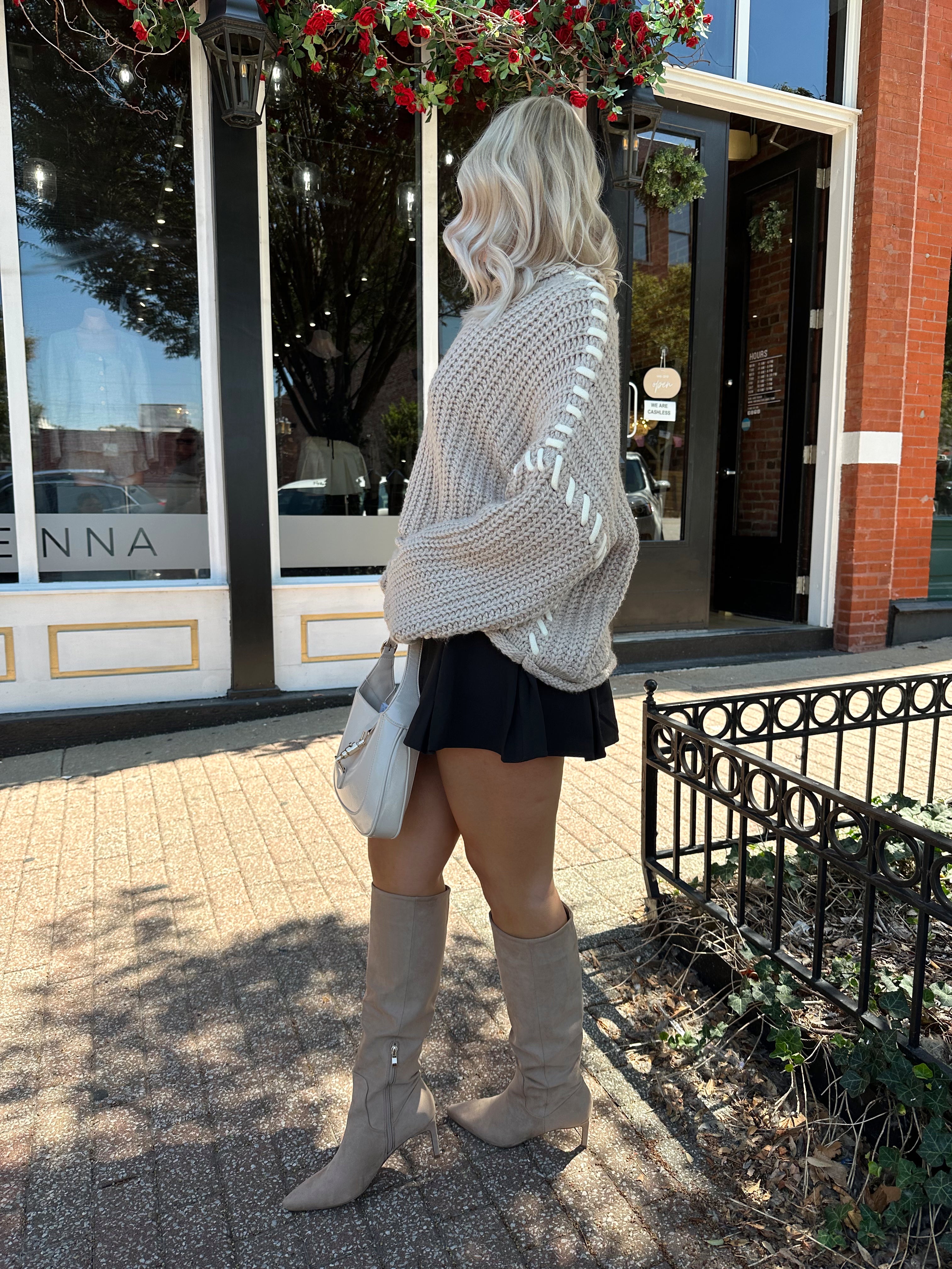 Woman wearing a grey knit oversized sweater with contrast lacing. 