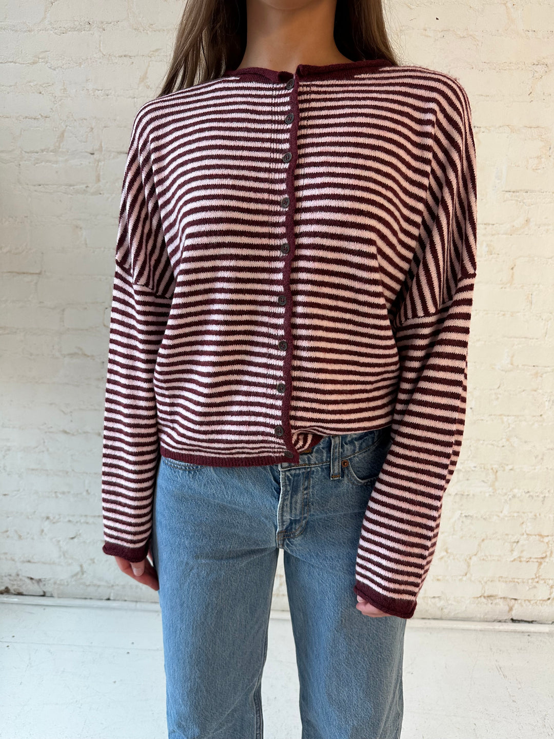 Woman wearing pink and burgundy striped knit button down cardigan and medium wash jeans. 