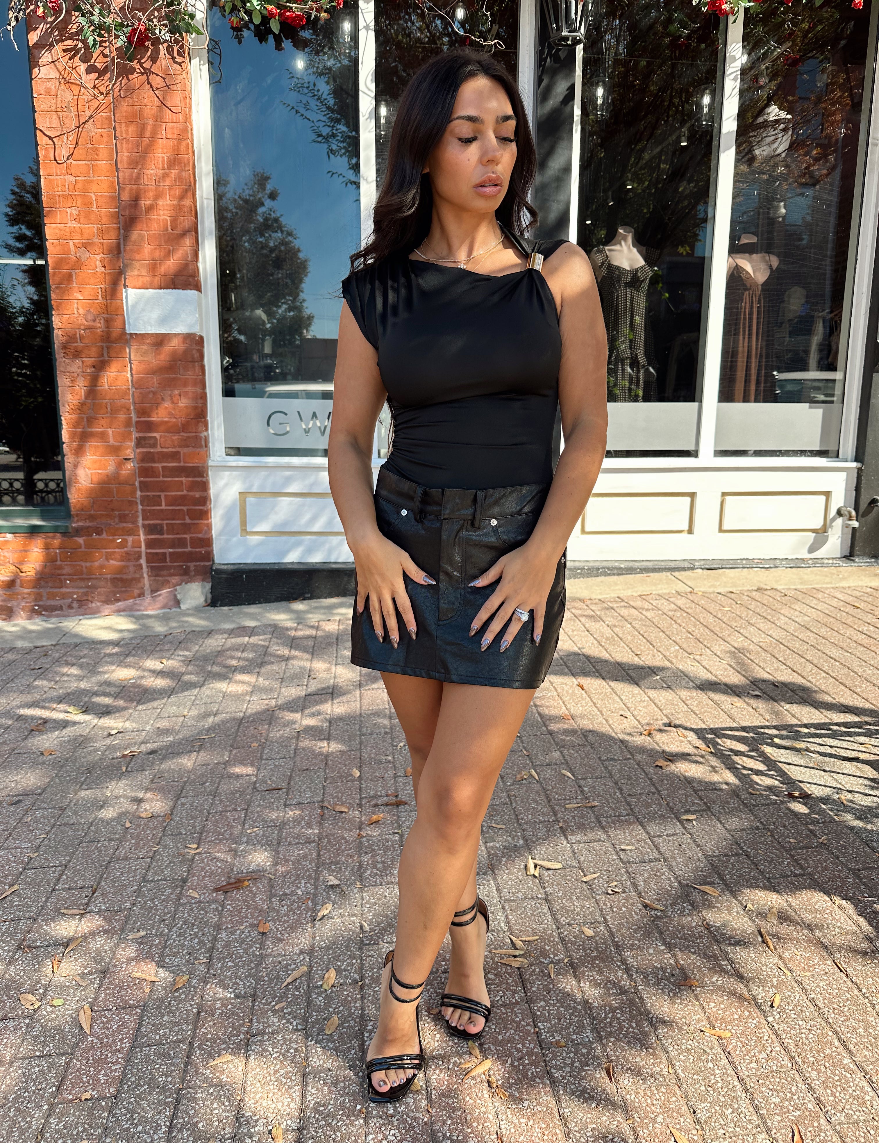 Woman wearing black asymmetrical shoulder top with gold piece detailing.