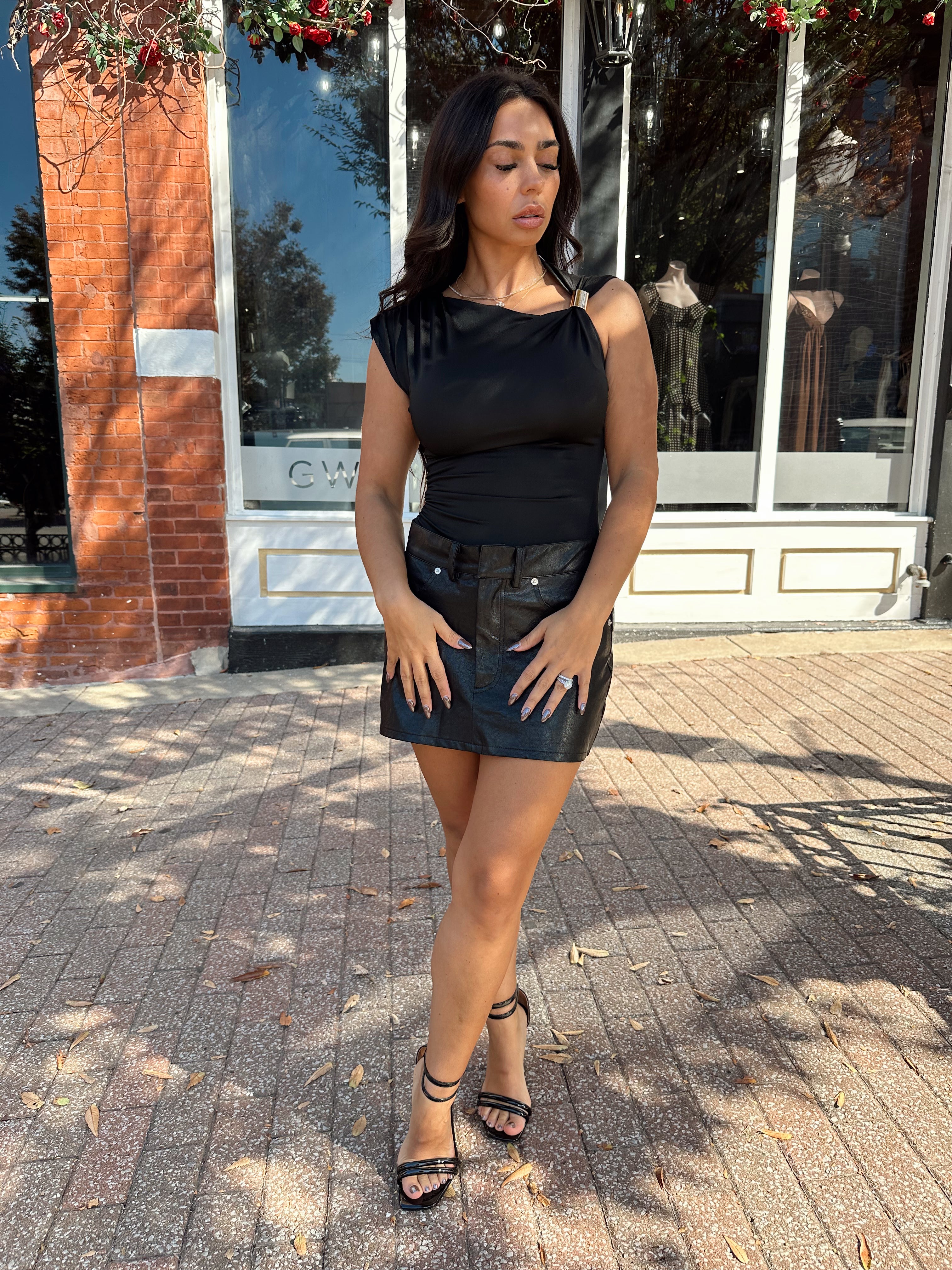 Woman wearing black asymmetrical shoulder top with gold piece detailing.