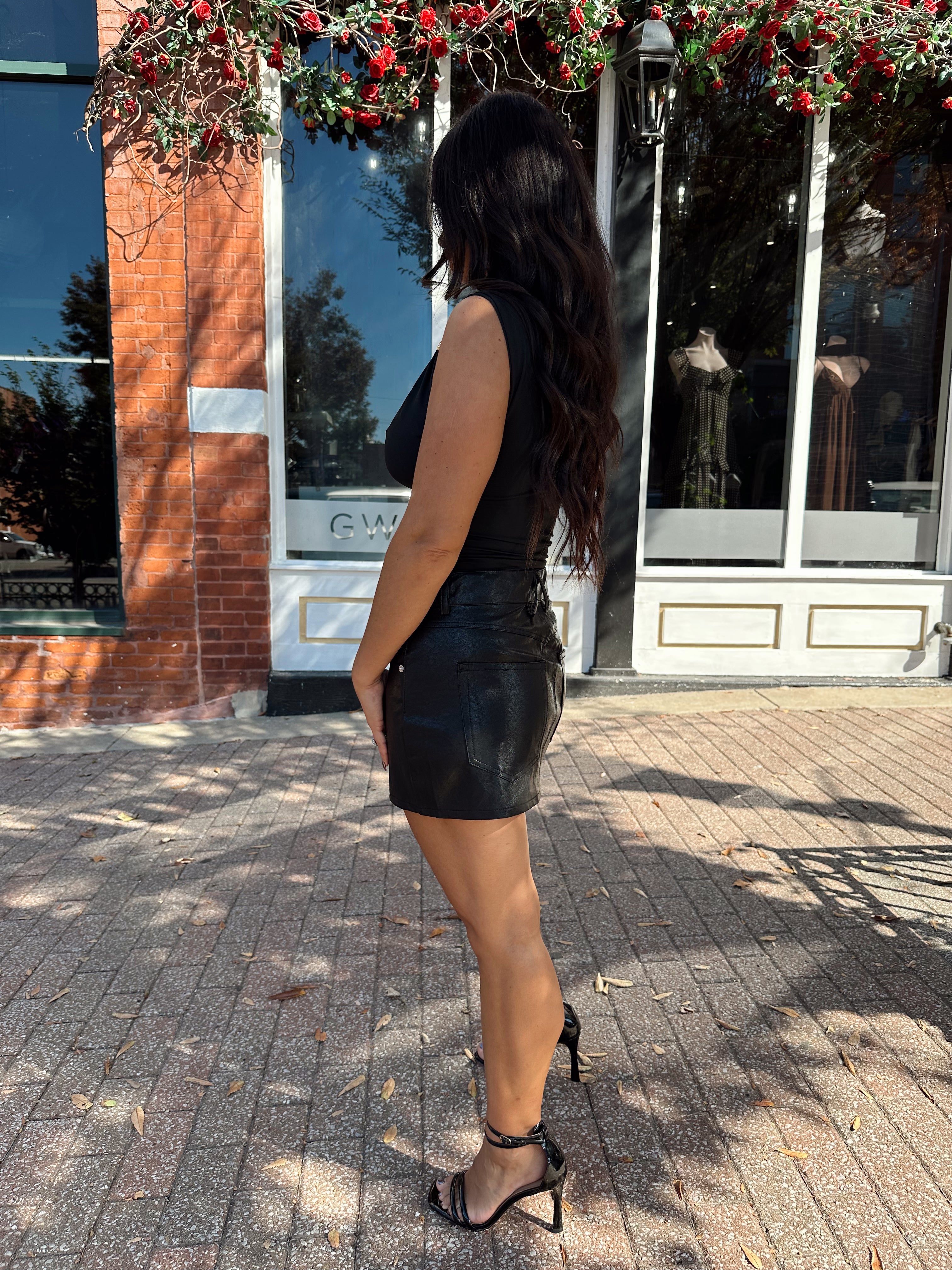 Woman wearing black asymmetrical shoulder top with gold piece detailing.