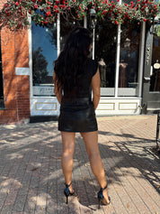 Woman wearing black asymmetrical shoulder top with gold piece detailing.
