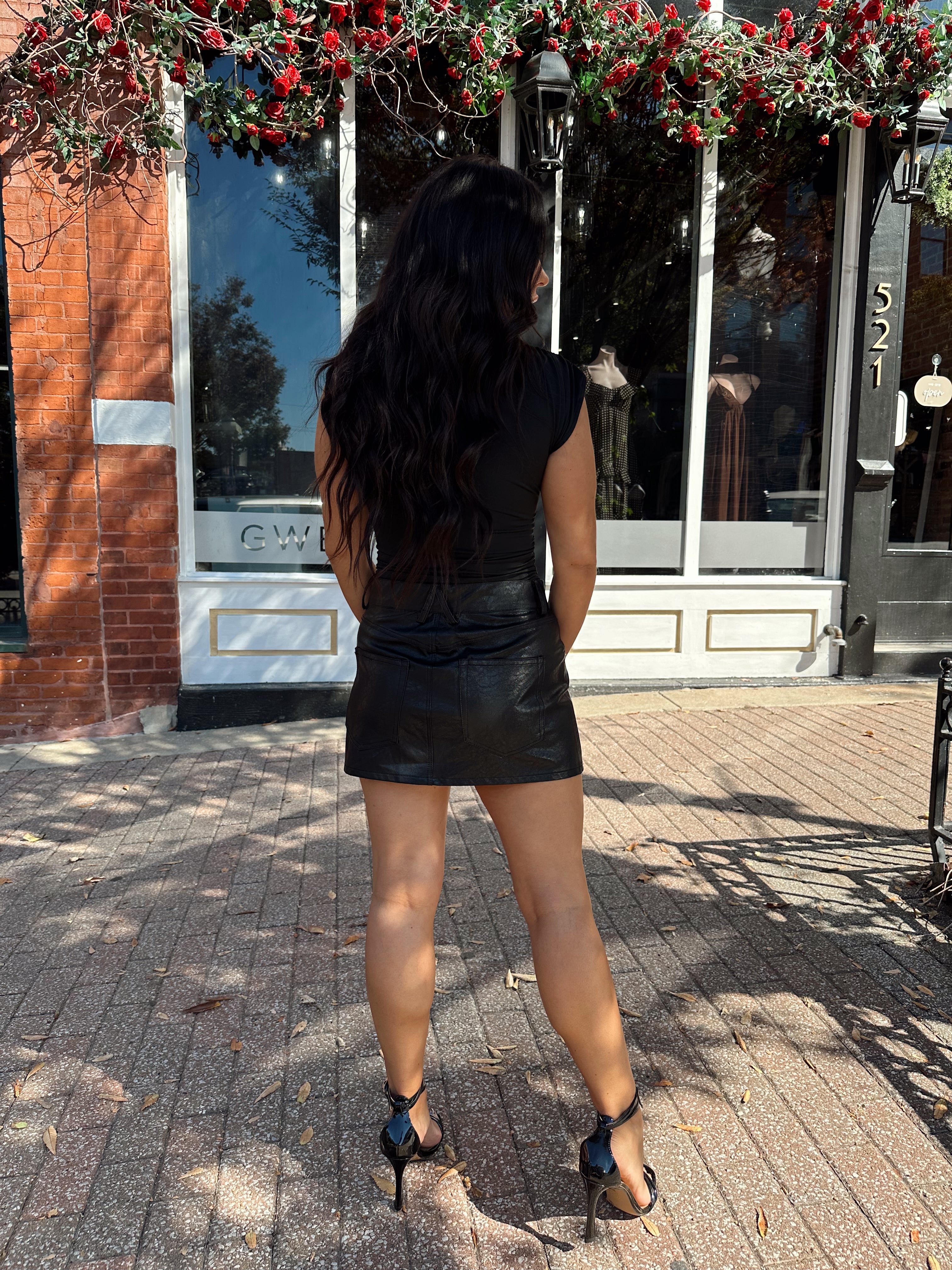 Woman wearing black asymmetrical shoulder top with gold piece detailing.