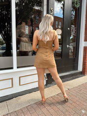 Woman wearing a tan suede sleeveless mini dress with adjustable straps.