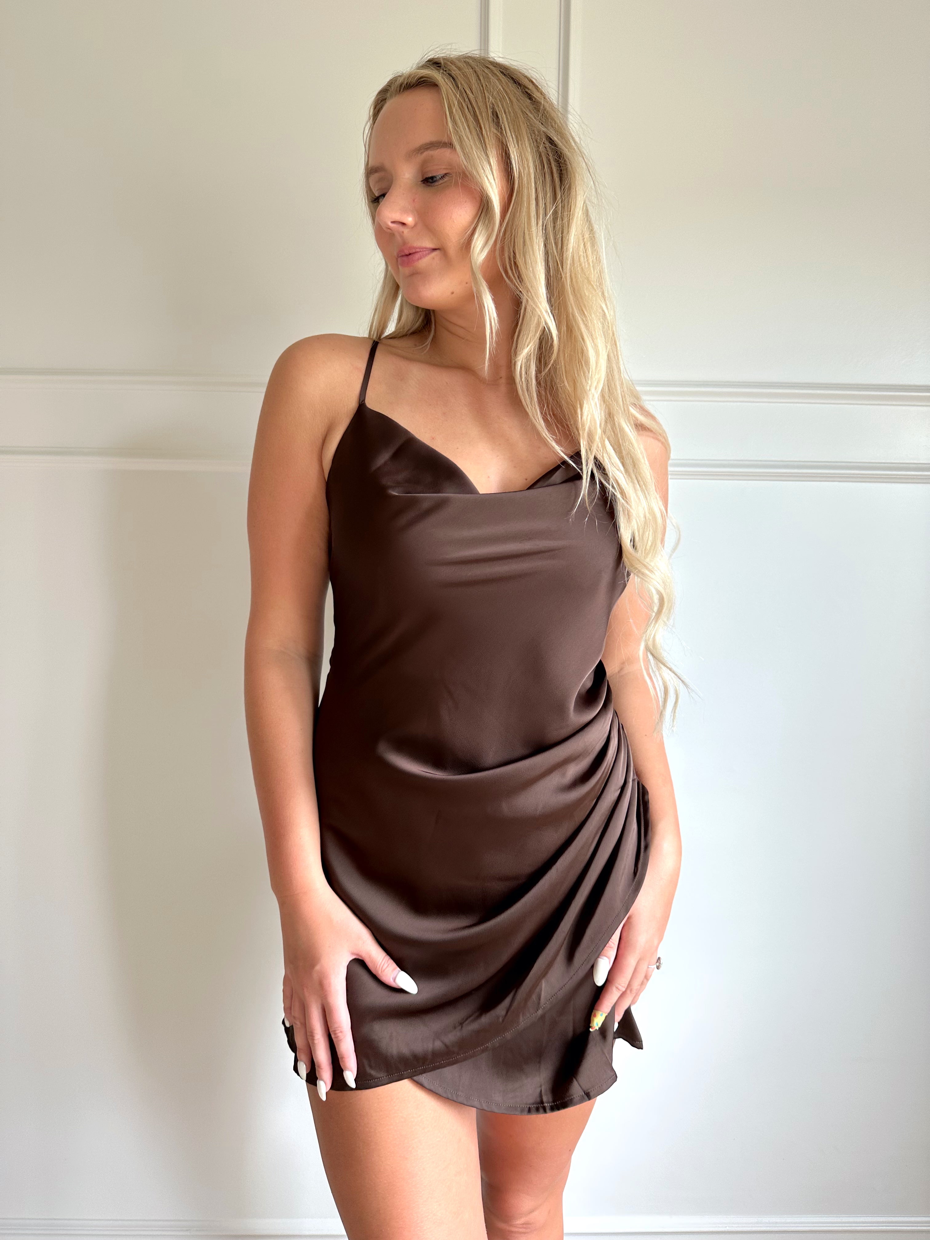 Woman wearing a dark brown satin mini dress with drapery midsection and cowl neckline. 
