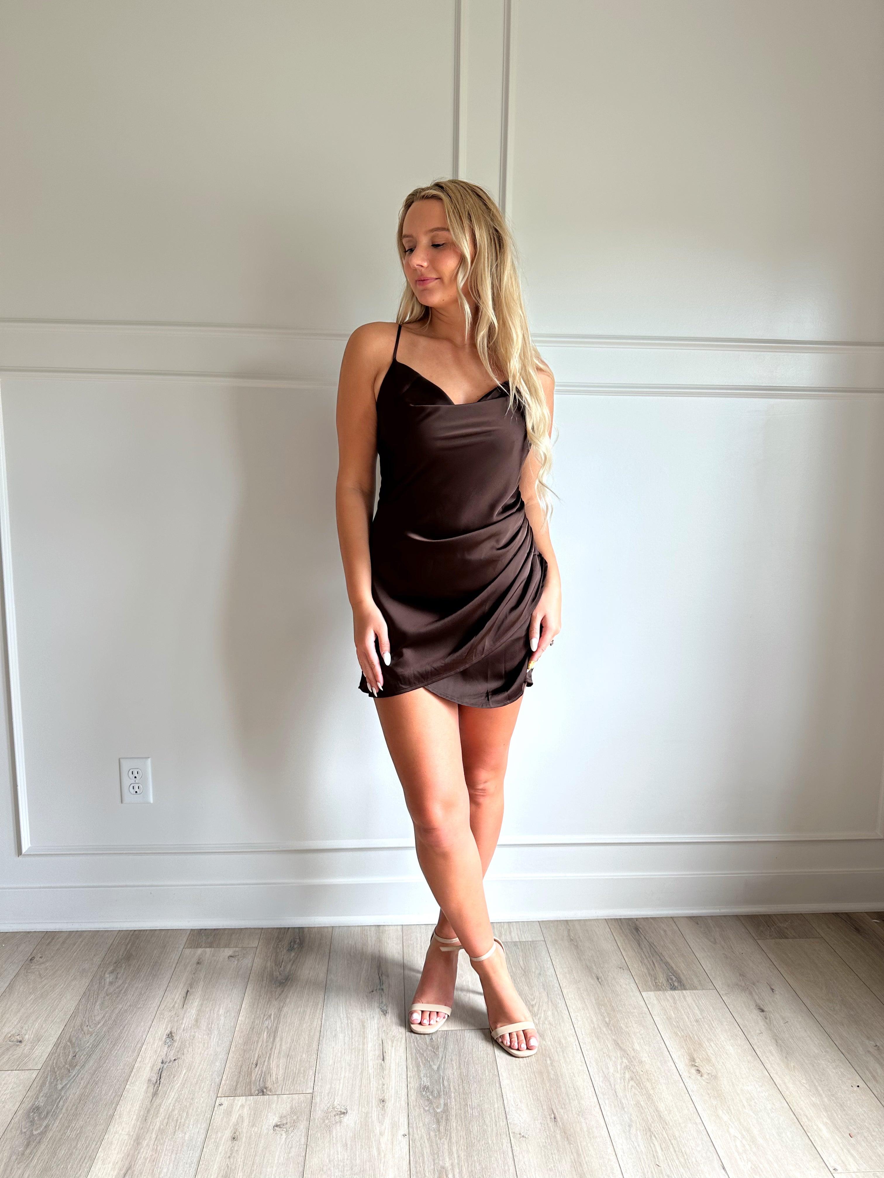 Woman wearing a dark brown satin mini dress with drapery midsection and cowl neckline. 