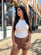 Woman wearing cream knit high neck sleeveless bodysuit and brown suede short. 