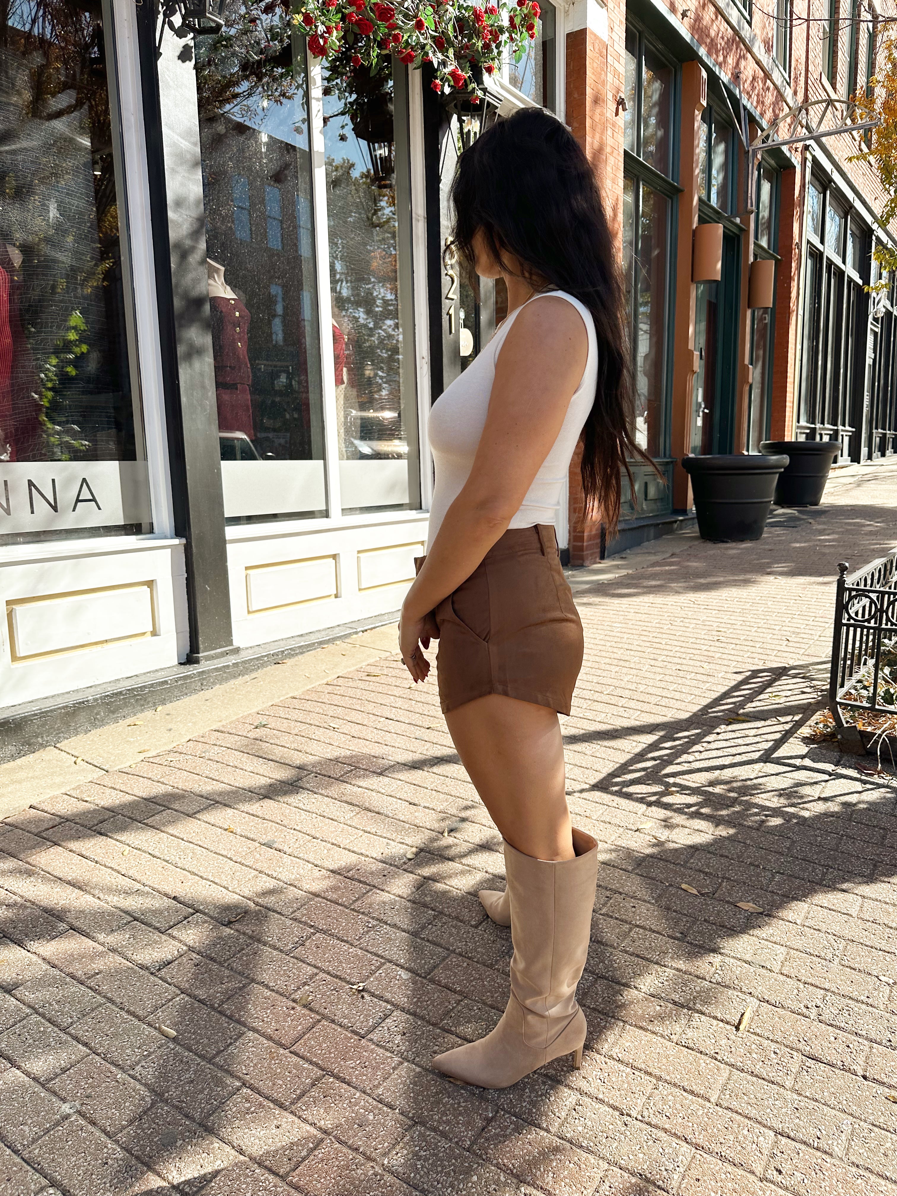 Woman wearing cream knit high neck sleeveless bodysuit and brown suede short. 