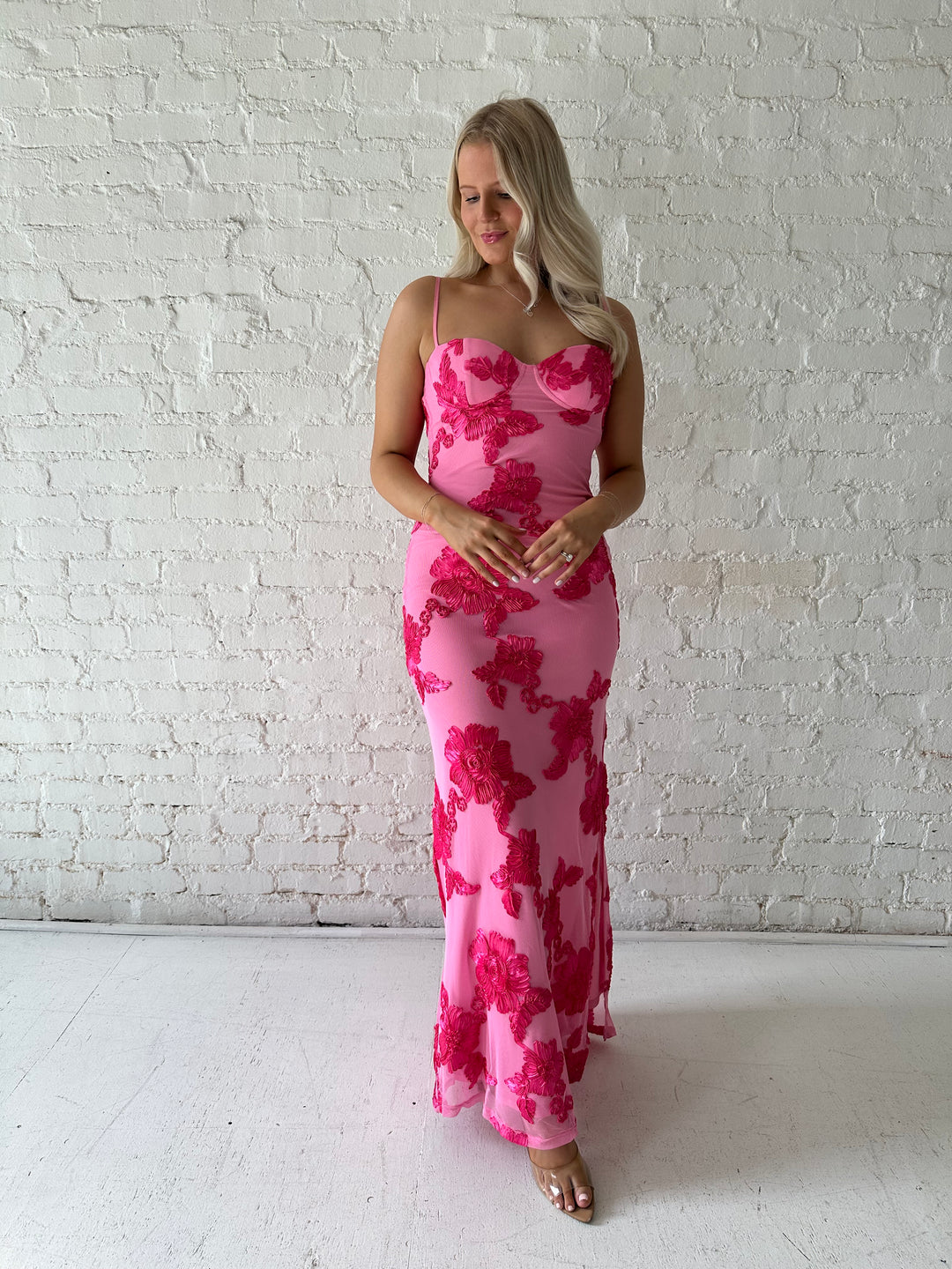 Woman wearing pink maxi dress with floral appliqué detail, and side slit.