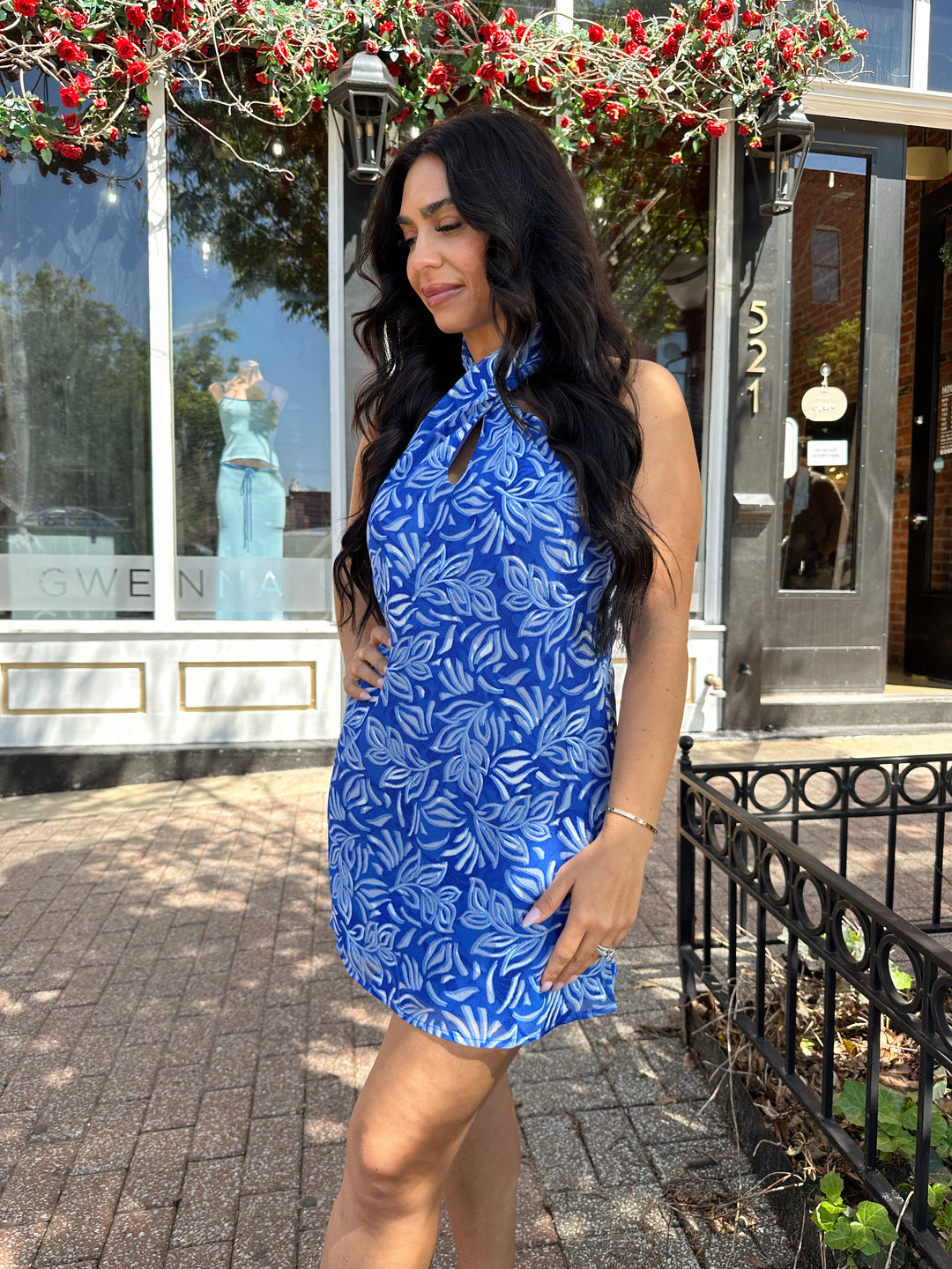 Woman wearing blue mini dress with white leaf pattern, and twisted halter neckline.
