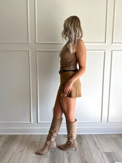 Woman wearing a tan ribbed tank top with raw trim and tan suede mini skirt. 