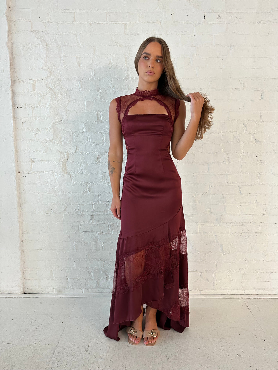 Woman wearing burgundy satin maxi dress with high lace neckline with cutout detailing, and lace bottom.