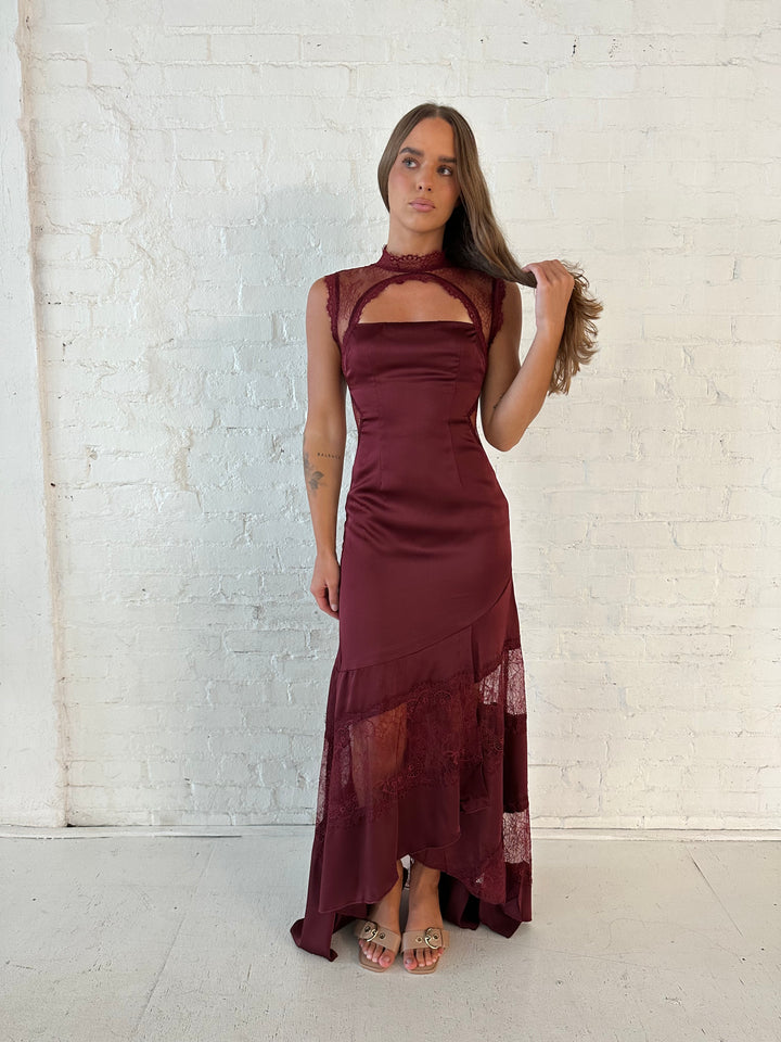 Woman wearing burgundy satin maxi dress with high lace neckline with cutout detailing, and lace bottom.