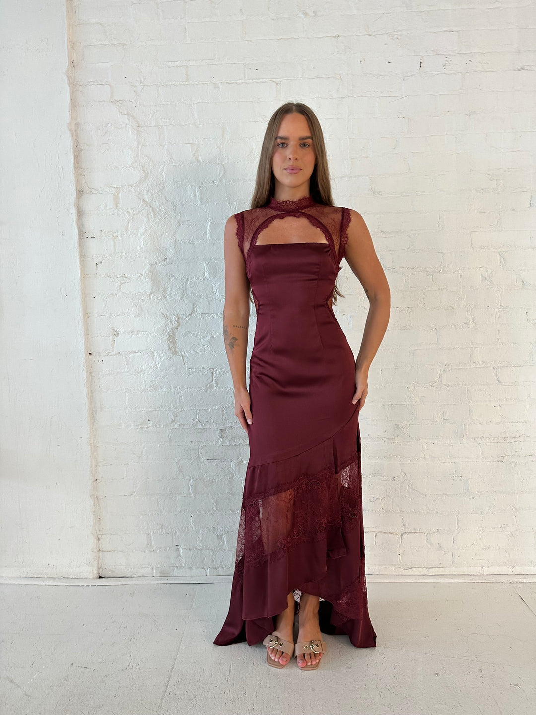 Woman wearing burgundy satin maxi dress with high lace neckline with cutout detailing, and lace bottom.