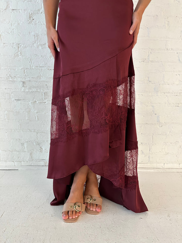 Woman wearing burgundy satin maxi dress with high lace neckline with cutout detailing, and lace bottom.