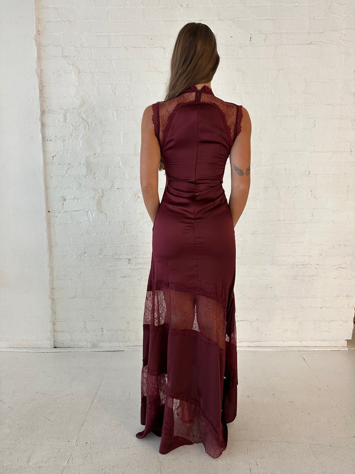 Woman wearing burgundy satin maxi dress with high lace neckline with cutout detailing, and lace bottom.