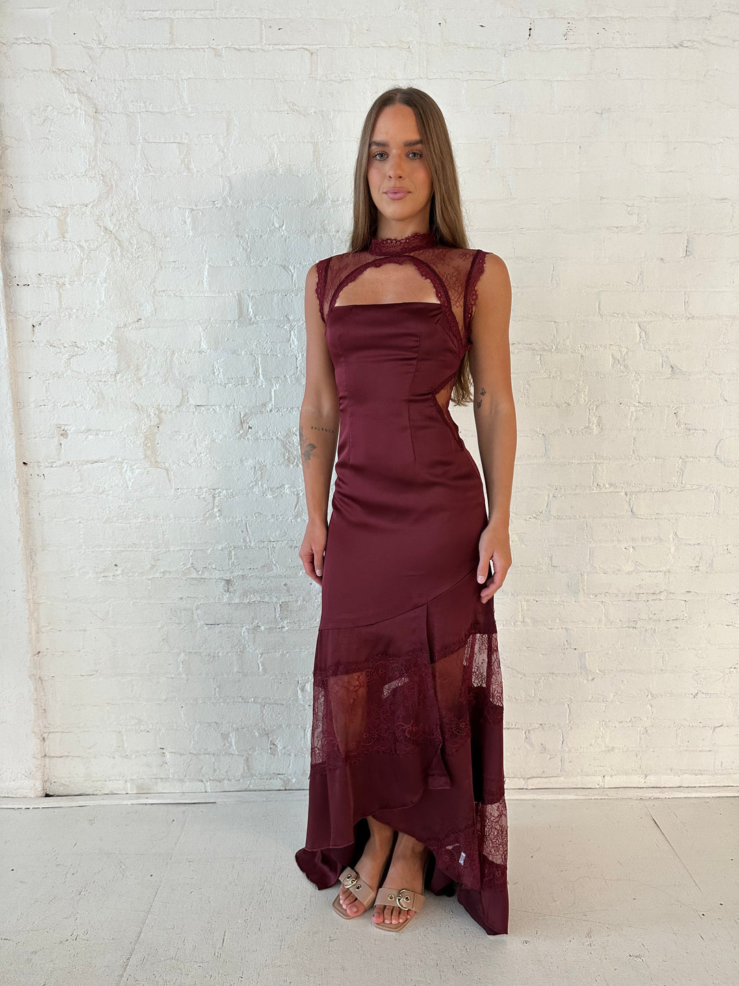 Woman wearing burgundy satin maxi dress with high lace neckline with cutout detailing, and lace bottom.