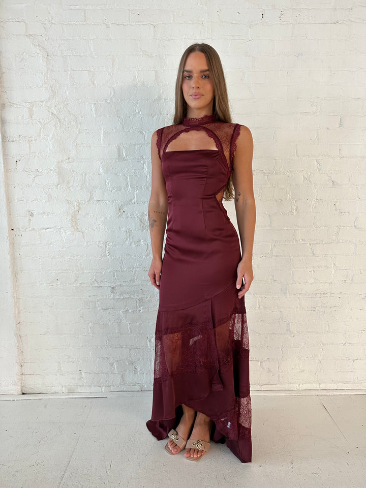 Woman wearing burgundy satin maxi dress with high lace neckline with cutout detailing, and lace bottom.