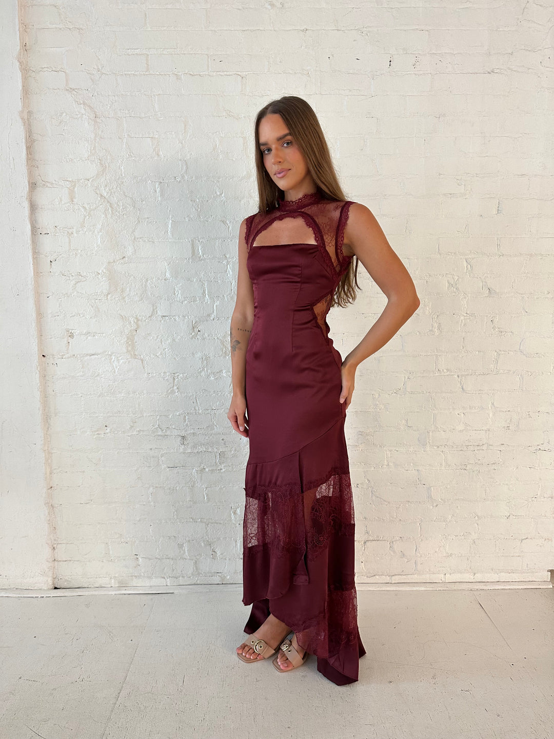 Woman wearing burgundy satin maxi dress with high lace neckline with cutout detailing, and lace bottom.