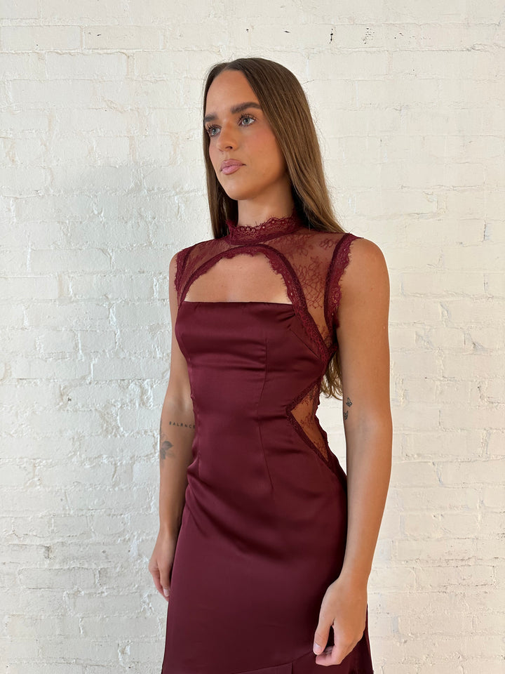 Woman wearing burgundy satin maxi dress with high lace neckline with cutout detailing, and lace bottom.