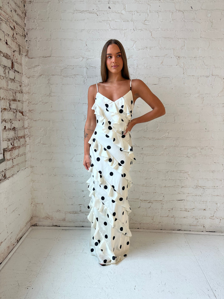 Woman wearing cream and black polka dot ruffle maxi dress with side slit.