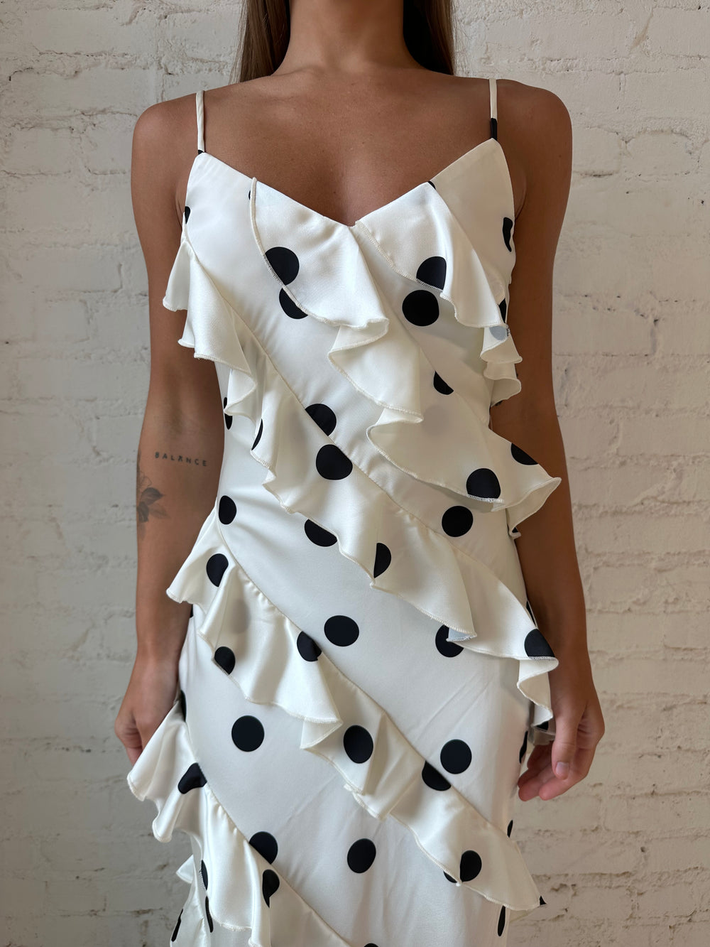 Woman wearing cream and black polka dot ruffle maxi dress with side slit.