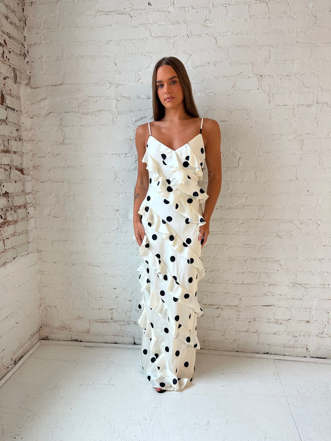 Woman wearing cream and black polka dot ruffle maxi dress with side slit.