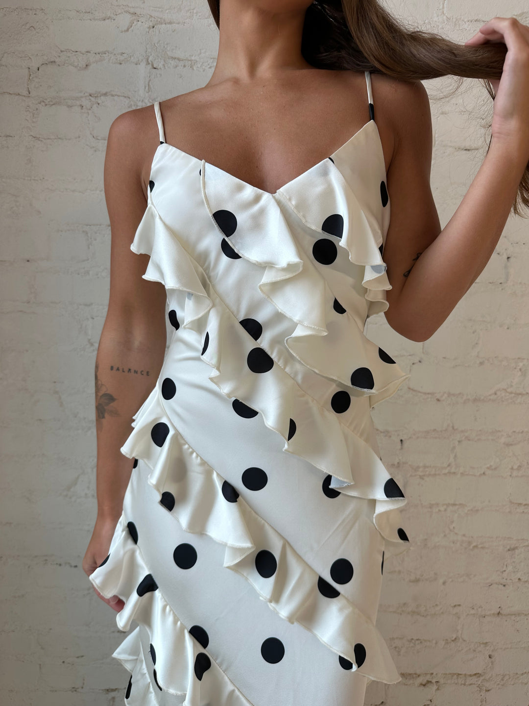 Woman wearing cream and black polka dot ruffle maxi dress with side slit.