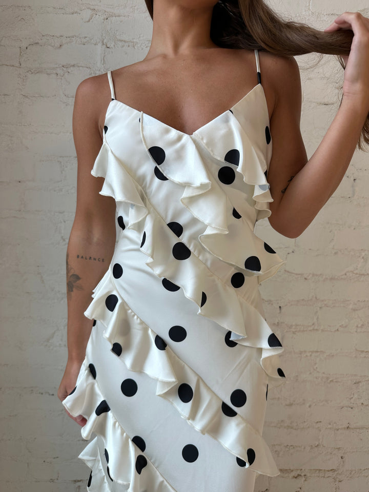 Woman wearing cream and black polka dot ruffle maxi dress with side slit.