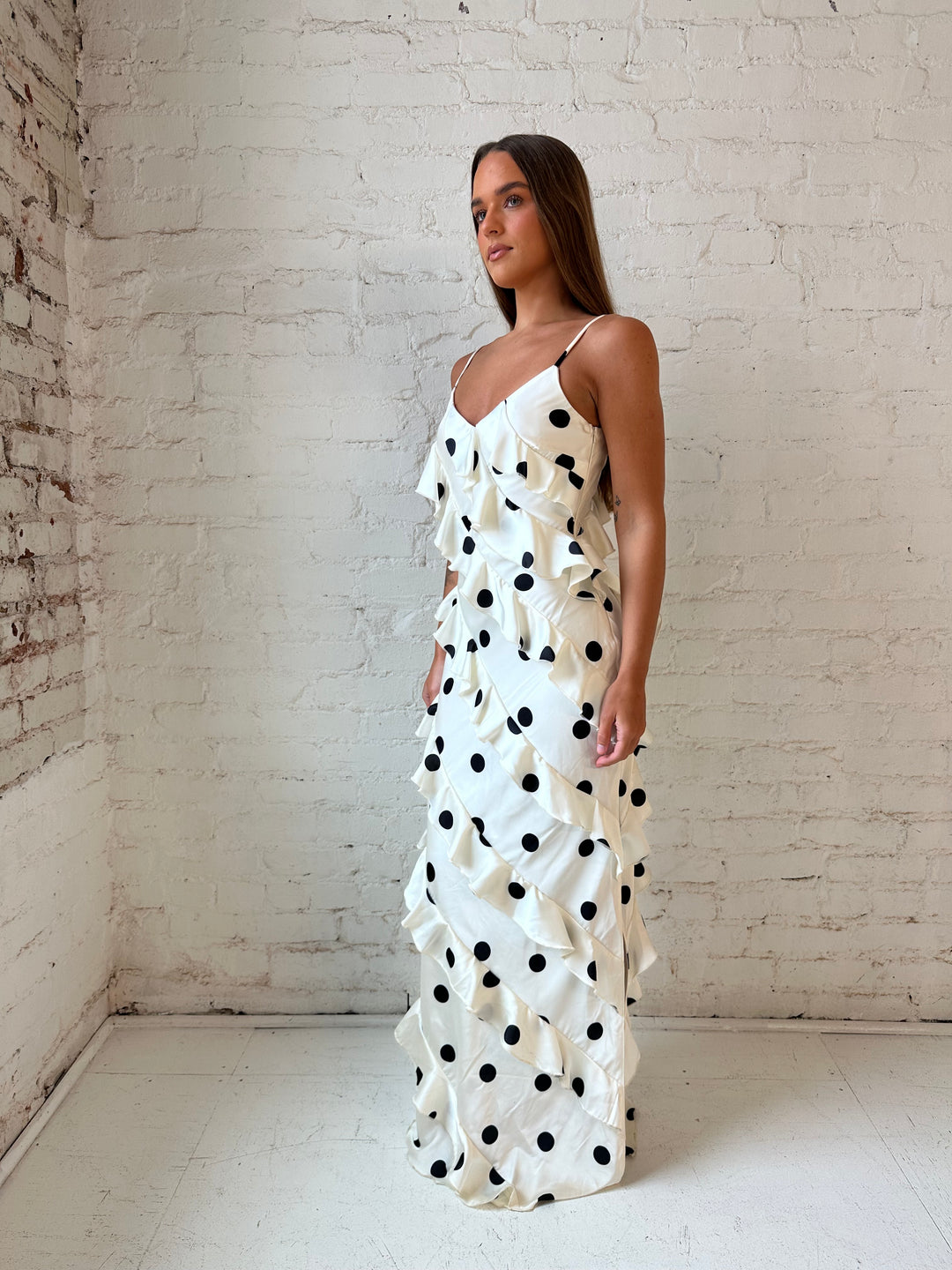 Woman wearing cream and black polka dot ruffle maxi dress with side slit.