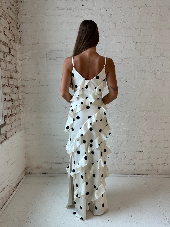 Woman wearing cream and black polka dot ruffle maxi dress with side slit.
