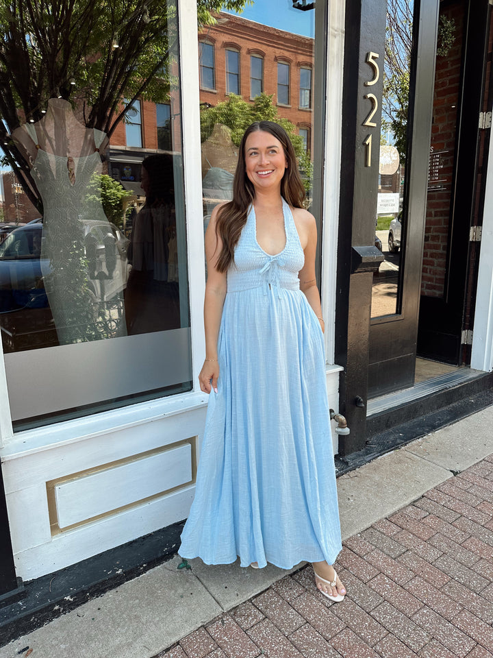 Woman wearing blue smocked midi dress with halter neck, tie detail, and pockets.